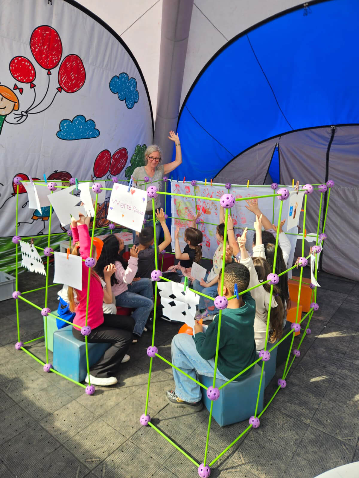 Workshopgruppe im WerteRaum-Pavillon mit Lehrkraft und Kindern im Kreis